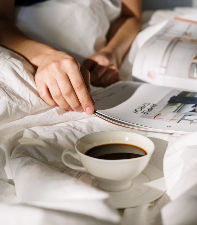 a person drinking tea and reading in bed