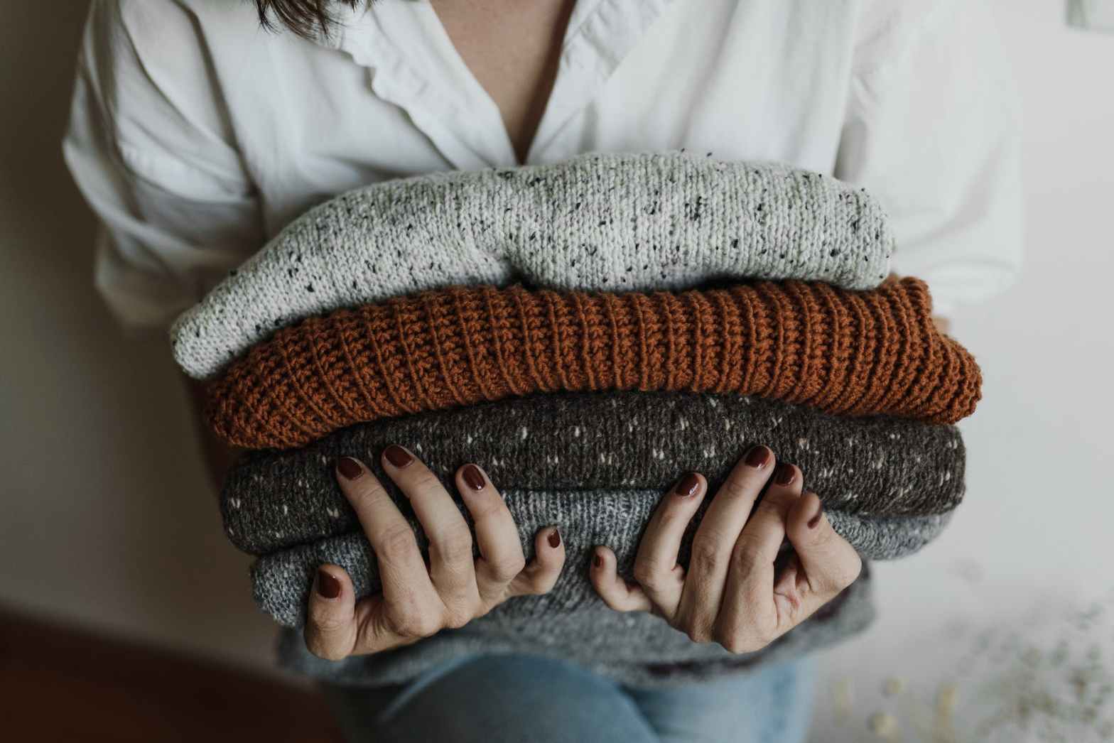 a close up shot of a person holding a stack of folded sweaters