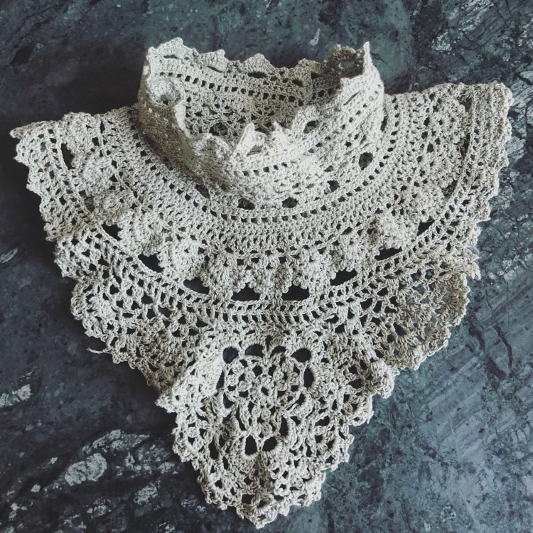 A light pale green lace collar in a victorian turtle neck style is lying flat on a marble table. 